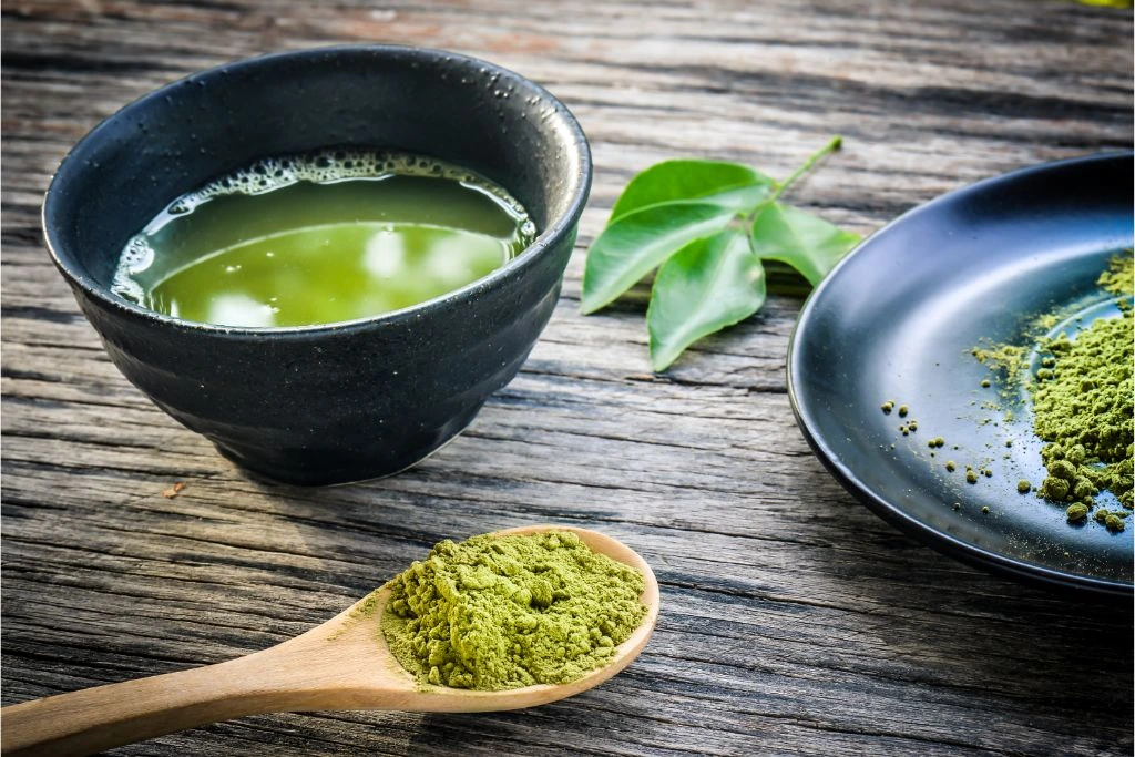matcha tea together with matcha powder on a wooden spoon situated in a wooden table