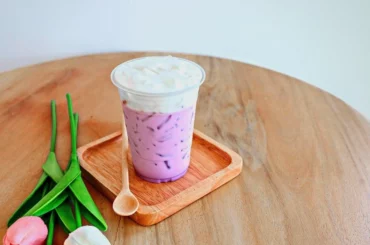 Taro Boba Milk Tea is placed on a wooded coaster with a flavor on the side