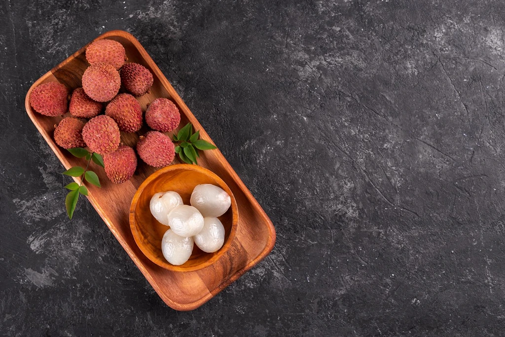 peeled and unpeeled lychees in a wooden serving plate on  a stone background