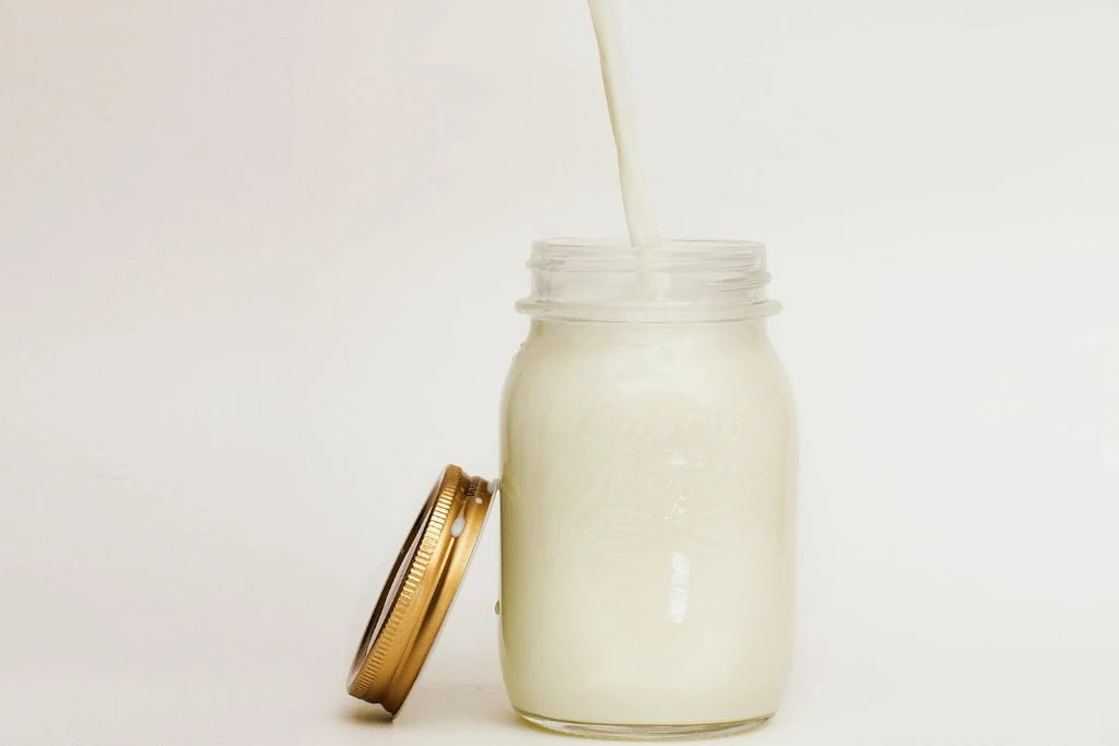 glass jar full of coconut milk tea with a paper straw with a jar cover beside on a white background