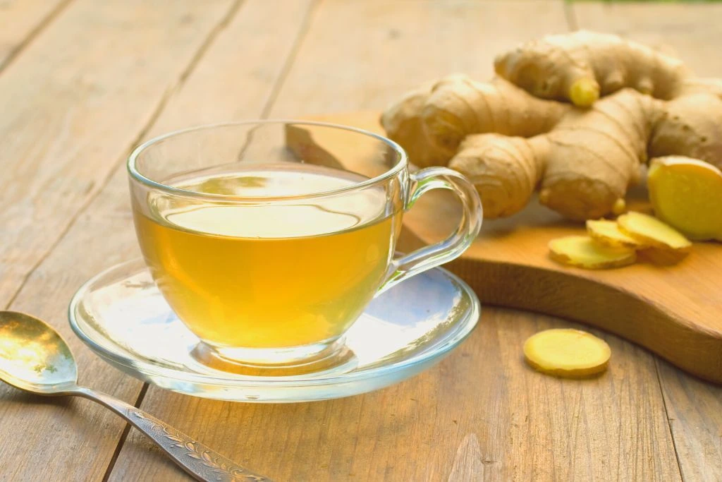 glass cup filled with ginger tea surrounded by ginger vegetable