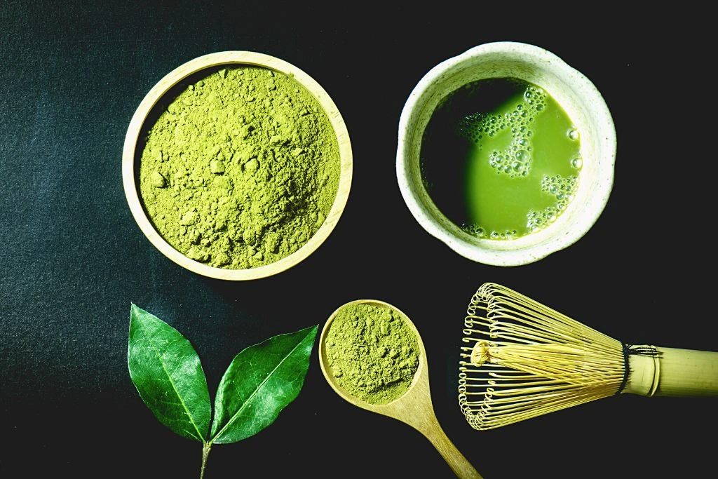 a small bowl of finely ground green matcha powder sits next to a spoon