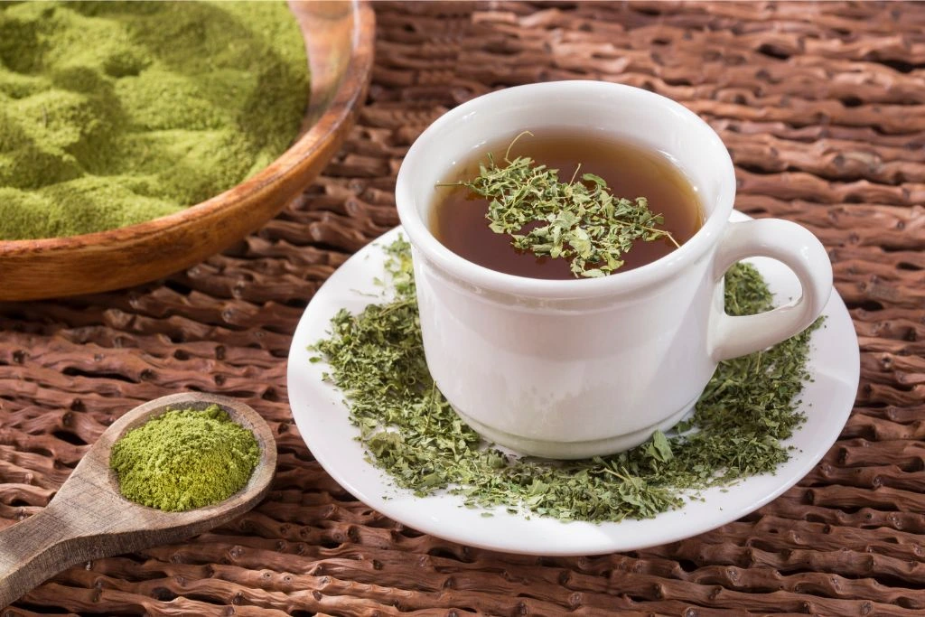a cup of hot moringa tea with dried and powdered moringa leaves on a wooden table