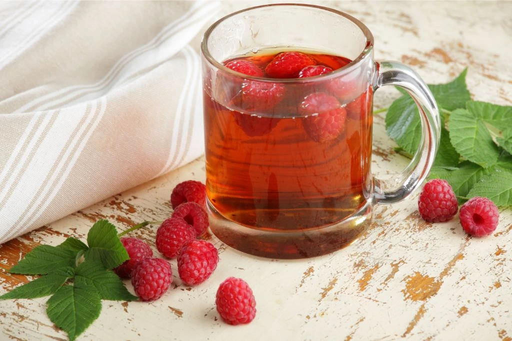 a mug of hot raspberry tea on a wooden table with fresh raspberries