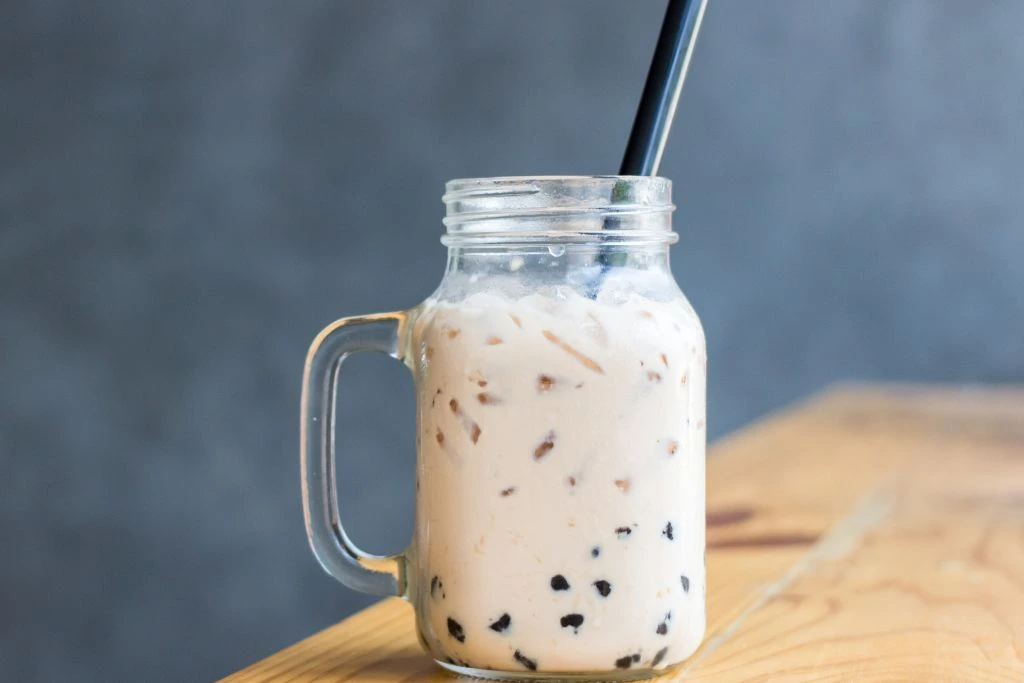 glass jar filled with white boba milk tea with a plastic straw on a blurry background