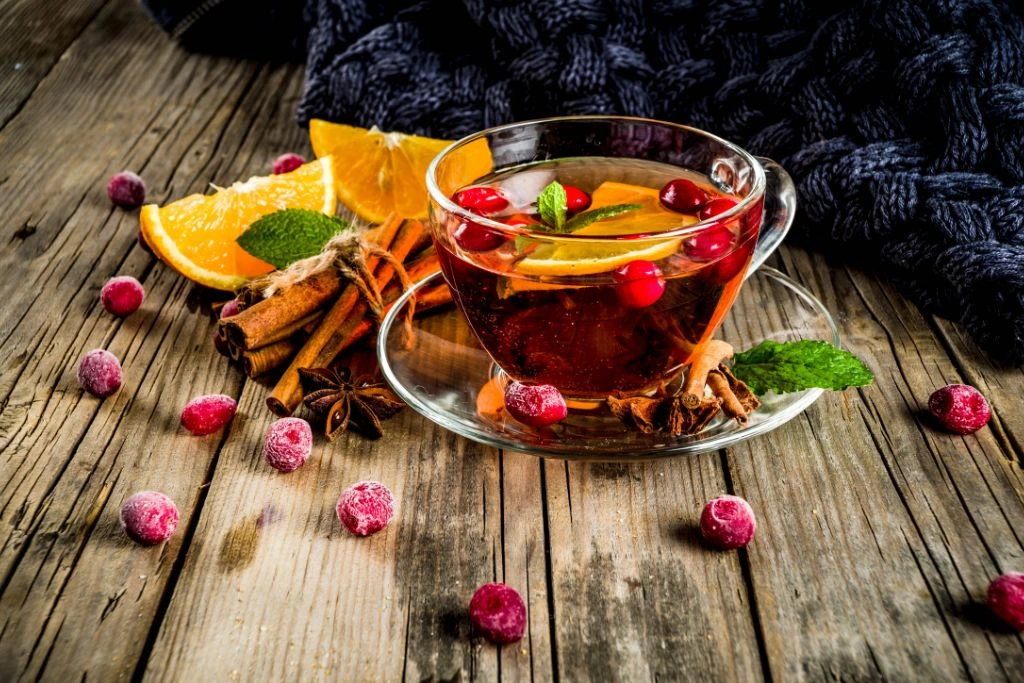 a cup of cranberry tea with lemon and cinnamon sticks on a wood table