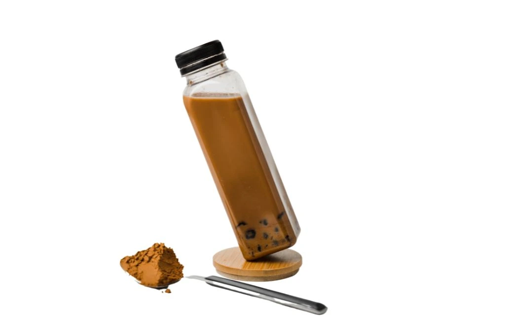 a bottle of chocolate milk tea and a spoon full of chocolate powder on a white background