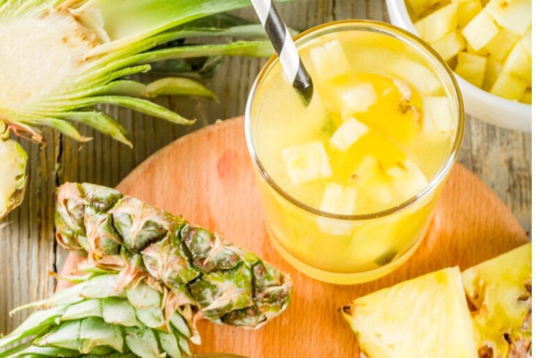 Pineapple green tea with straw and pineapple fruits and chunks at the background