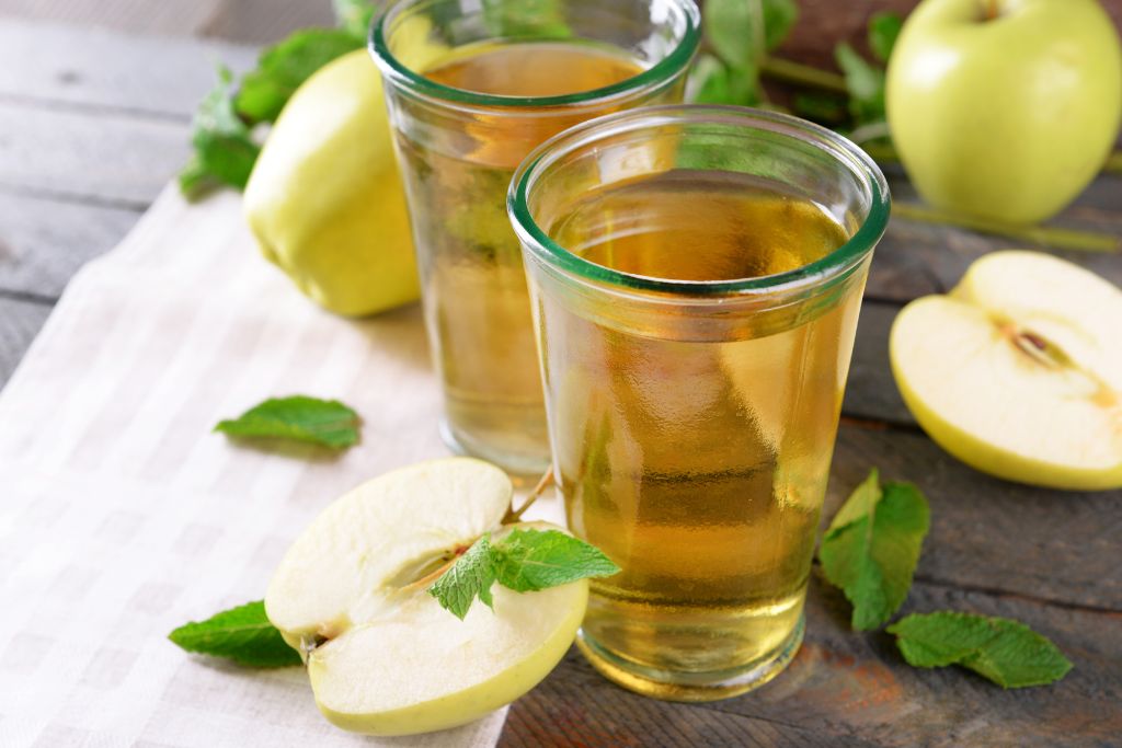 two cups of apple mint tea together with fresh mint leaves and apple slices on table