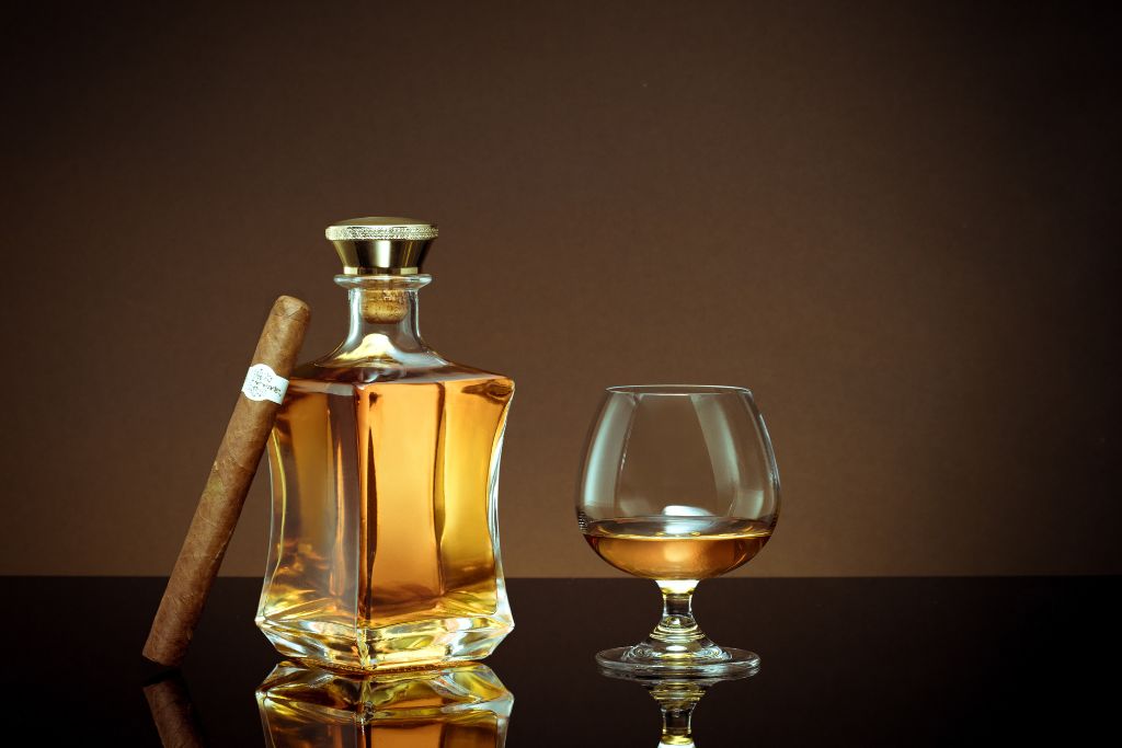 rum bottle together with wine cup and cigar on brownish background