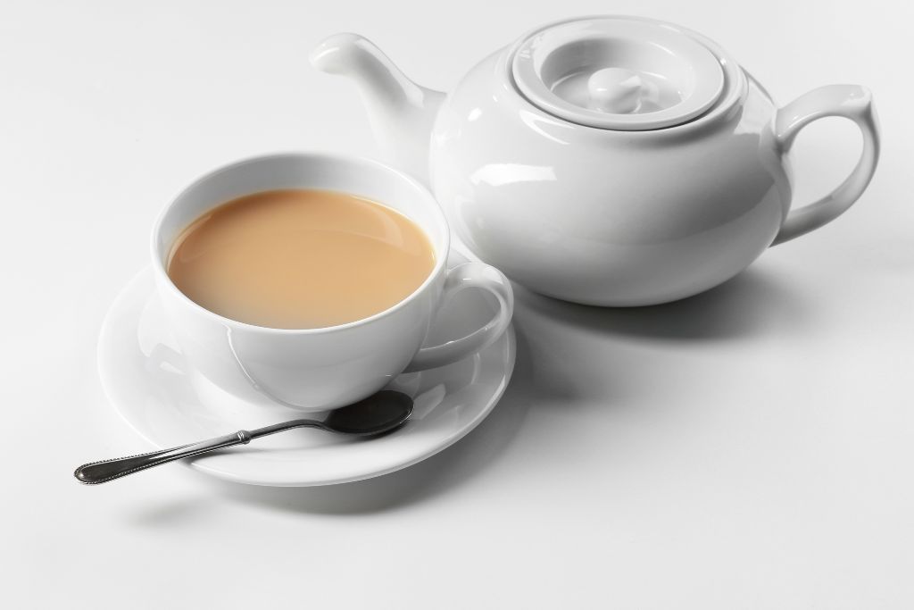 tea with milk served on a teacup together with a white teapot on white background