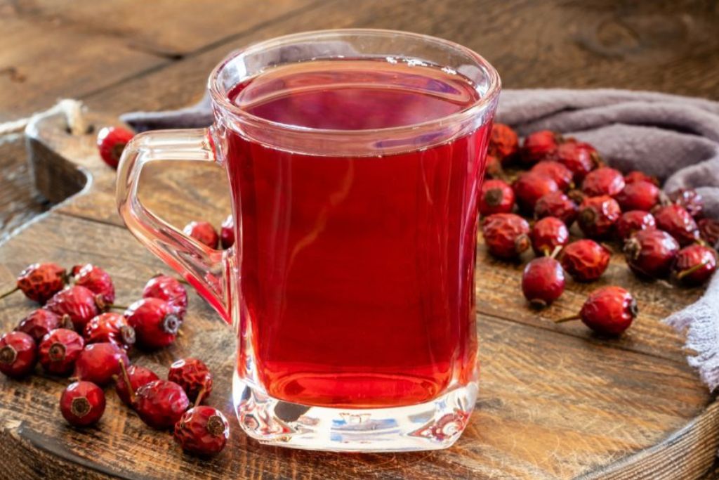 a glass of rose hip tea with rose hip fruits on the side